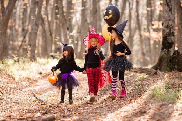 Trois petites filles en costumes de sorcière rient à travers la forêt d'automne avec des paniers de bonbons