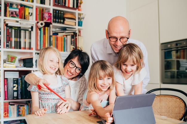 Trois petites soeurs à l'intérieur à la maison à l'aide d'une table assise sur tablette supervisée par les parents