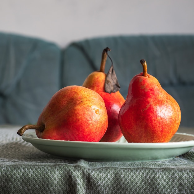 Photo trois poires rouges sur une plaque verte debout sur une table couverte