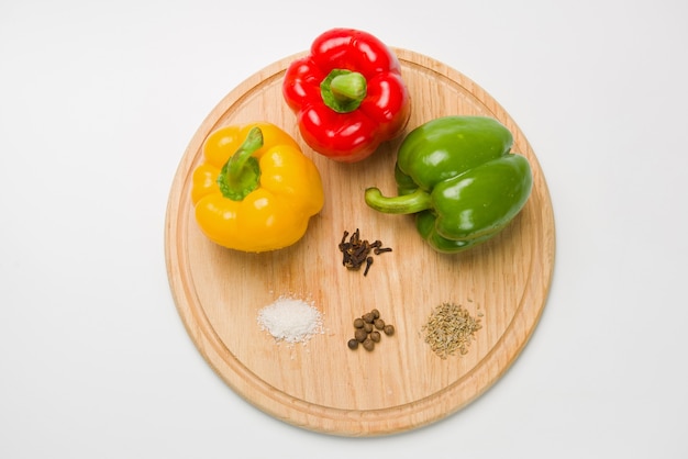 Trois poivrons bulgares de couleurs différentes se trouvent dans une rangée sur une planche à découper en bois. Poivrons avec diverses épices. d'en haut.