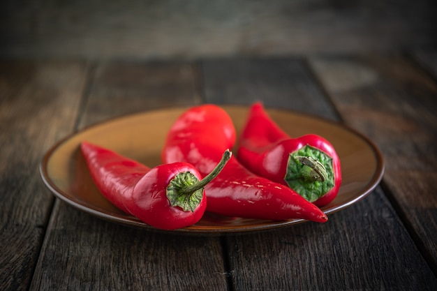 Trois poivrons rouges appétissants sur une plaque en céramique sur une table de cuisine en bois