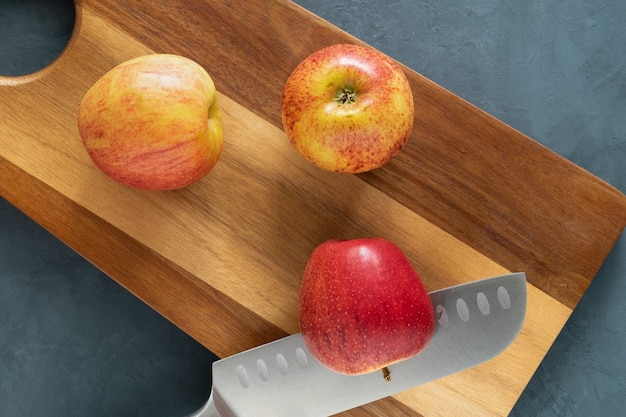 Trois pommes mûres rouges et un grand couteau de chef se trouvent sur une planche à découper