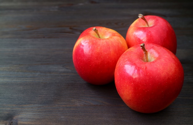 Photo trois pommes rouges sur une table en bois de couleur foncée