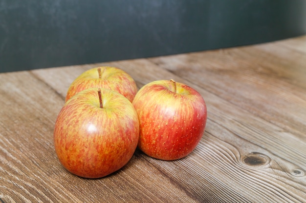 Photo trois pommes sur une table en bois et avec un fond sombre.