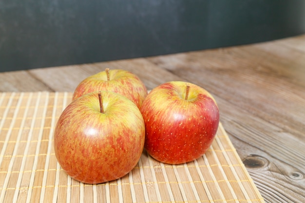 Trois pommes sur un tapis en bois, avec un fond sombre.