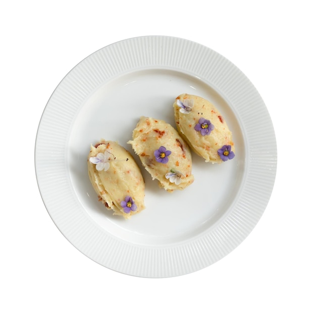 Trois pommes de terre écrasées avec des fleurs violettes et blanches sont sur une assiette