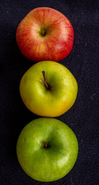 Trois pommes, une verte et deux rouges et jaunes sur fond sombre.