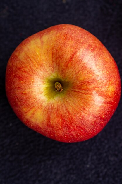 Trois pommes, une verte et deux rouges et jaunes sur fond sombre.