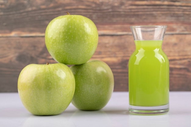 Trois pommes vertes fraîches avec un pichet en verre de jus sur une table en bois.