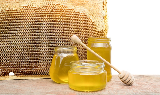 trois pots de miel et un cadre d'abeille sur fond blanc