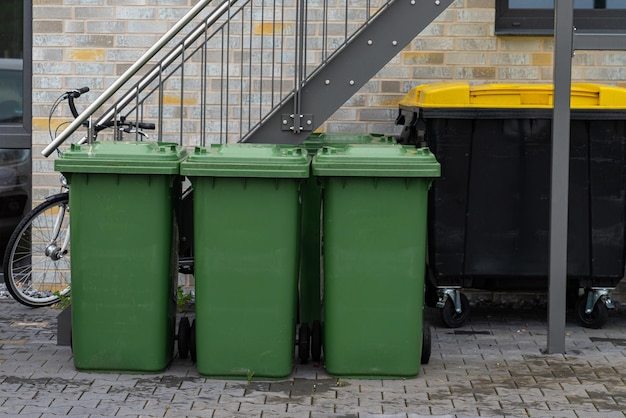 Trois poubelles vertes devant un immeuble résidentiel