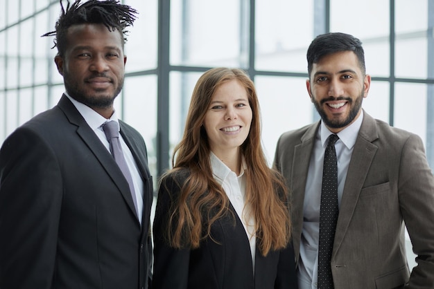 Trois professionnels en costumes formels debout pour l'appareil photo à l'intérieur et souriant con amitié d'entreprise