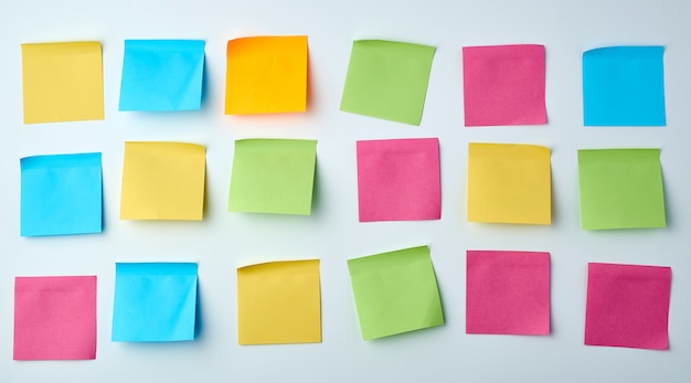 Photo trois rangées d'autocollants multicolores en papier carré blanc sur un mur blanc