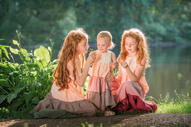 Trois sœurs aux cheveux roux en longues robes de lin soufflent des bulles dans le parc le jour d'été ensoleillé