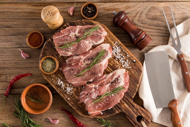 Trois steaks de porc de ferme sur une planche de cuisine rustique en bois avec des ingrédients pour la cuisson table rustique vue de dessus