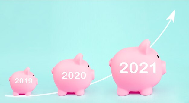 Photo trois tirelire rose avec flèche blanche hologramme numérique et signe de l'année 2021 sur fond bleu. croissance des investissements. épargne financière et économie bancaire