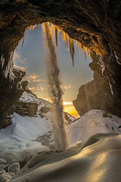 Trois touristes alpinistes devant la cascade gelée de Kvernufoss avec de la neige et des stalagmites