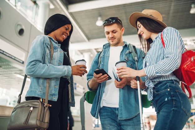 Trois touristes avec des bagages en attente de départ et boit du café à l'aéroport, voyageur masculin utilisant un téléphone mobile.