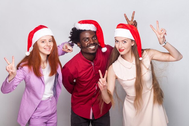 Trois travailleurs du bonheur en bonnet rouge, montrant un signe v à la caméra et souriant à pleines dents. Prise de vue en studio