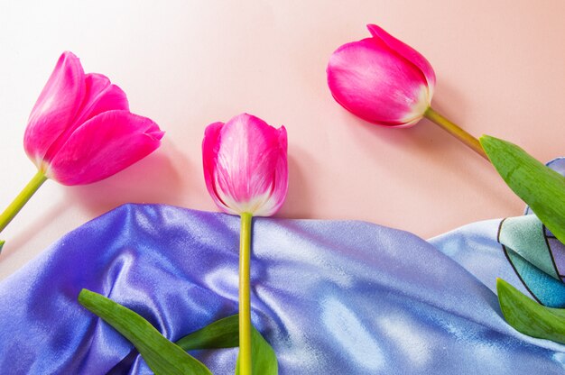 Trois tulipes roses reposent sur un foulard en soie lilas, vue du dessus