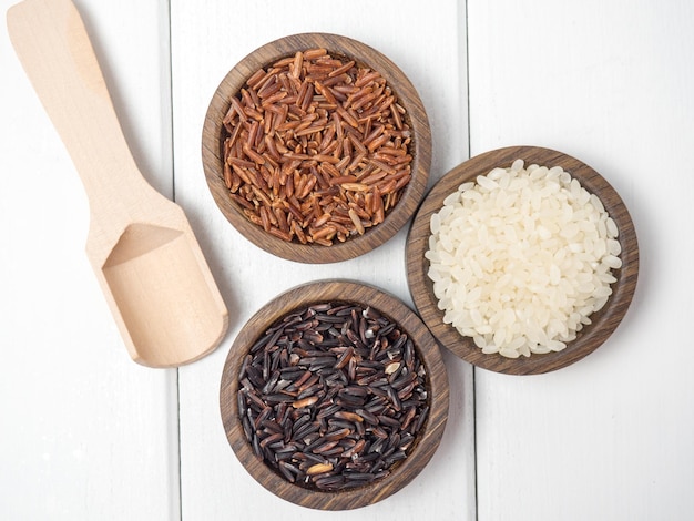 Trois types de riz dans des bols en bois sur une table en bois blanc espace de copie de riz noir et blanc rouge