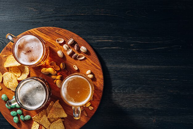 Trois verres de bière artisanale chère, classique et non filtrée et sombre dans un verre sur la table avec une collation de chips d'arachide et de pistache et de nachos