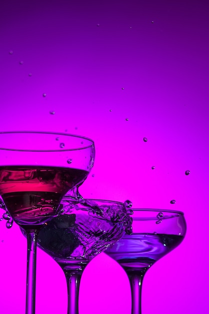 Trois verres farcis de vin debout sur la table au studio. Éclairage aux couleurs vives et lumineuses. Tendance en 2018 Ampoule Ultra Violet. Décoration d'art avec ton de couleur mystique