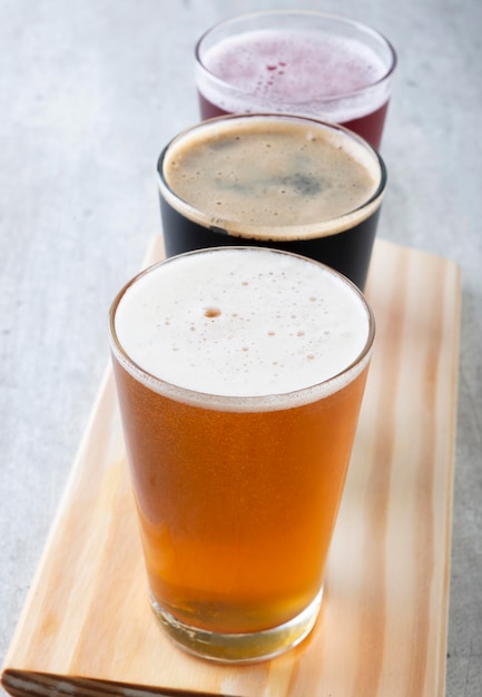 Trois verres de pinte de bière sur une planche en bois Bière dorée foncée et rouge