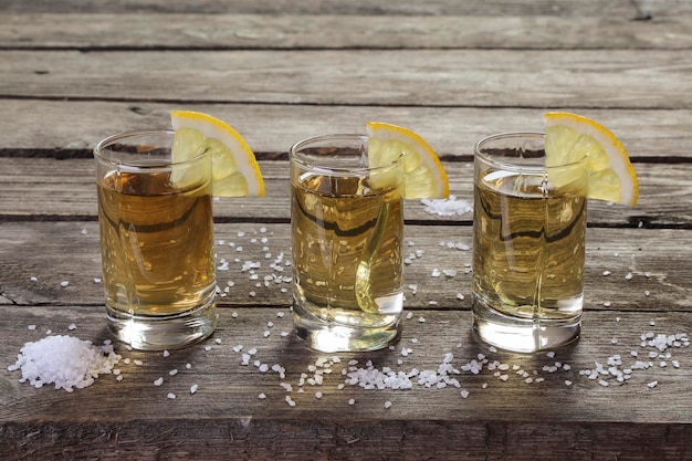 Photo trois verres de tequila au citron et au sel sur une table en bois