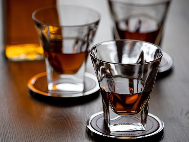 Trois verres de whisky droit sur des sous-verres sur un dessus de bar en bois