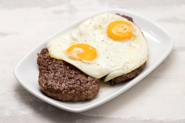 Trois viandes hachées frites avec œuf au plat sur plaque blanche