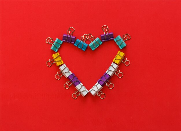 Trombones de bureau en métal multicolore formant forme de coeur sur fond rouge. Concept Saint Valentin.
