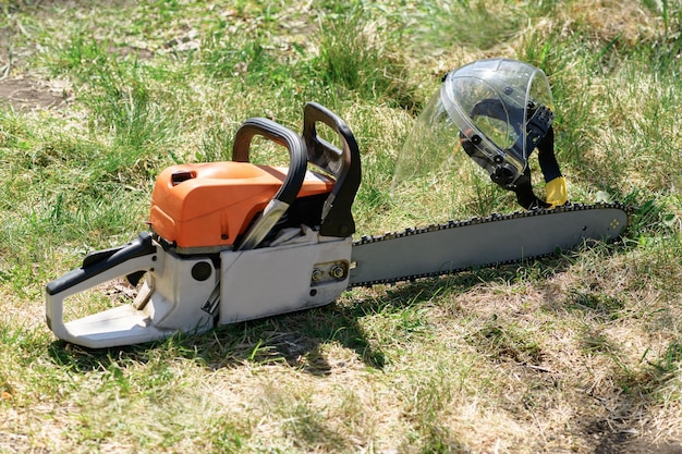 Tronçonneuse et écran facial protecteur, casque sur l'herbe verte par une journée ensoleillée. Le concept est de couper des arbres