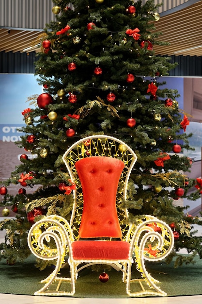 Trône pour le Père Noël sous le sapin de Noël Guirlande de boules colorées, lampes rougeoyantes et baies rouges sur les branches sont saupoudrés de neige Fond traditionnel festif et harmonieux pour le Nouvel An