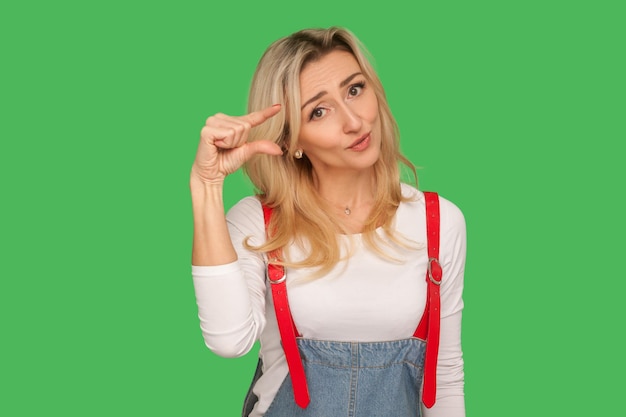 Photo trop petit portrait d'une femme adulte insatisfaite avec un regard d'excuse montrant un petit geste pouce ou centimètre déçu par la taille minimale prise de vue en studio intérieur isolée sur fond vert