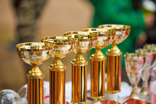 Trophées d'or de champion en gros plan, mise au point sélective. De nombreuses coupes de trophées dorées brillantes alignées en rangée sur la table. Trophées pour le leadership des champions en tournoi, compétition de sports de plein air