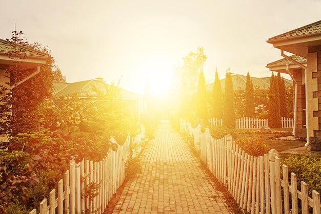 Trottoir entre cottages et jardins au soleil levant petites clôtures autour de la route belles maisons et arbres s...