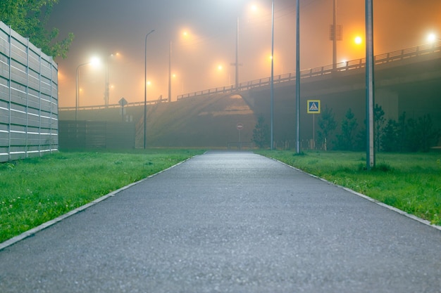 Trottoir vide entouré de pelouse menant à un pont dans le brouillard avec éclairage