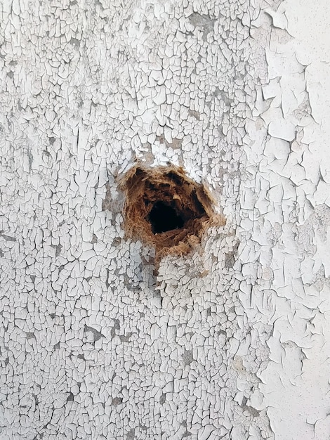 Un trou dans un mur peint en bois d'un gros plan de balle couvrant la peinture craquelée