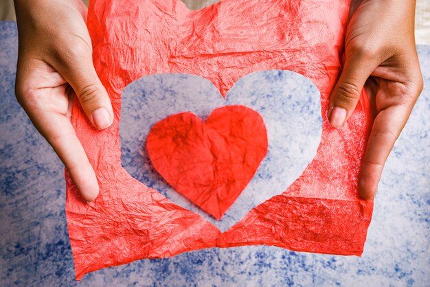 Trou rouge en forme de coeur déchiré à travers le papier dans les mains de la femme, isolé sur fond bleu