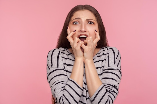 Trouble anxieux. Portrait d'une femme stressée et nerveuse en sweat-shirt rayé qui se ronge les ongles, une personne névrosée qui a l'air effrayée, terrifiée par les problèmes. studio d'intérieur tourné isolé sur fond rose