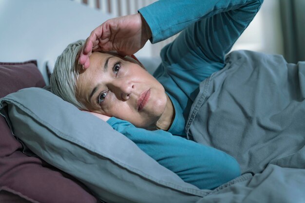 Photo trouble du sommeil inquiète femme âgée souffrant d'insomnie ayant des maux de tête touchant son front