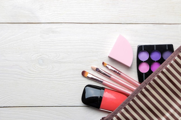 Trousse de maquillage Cosmétiques pour femmes dans un sac à cosmétiques et pinceaux de maquillage sur une vue de dessus de fond en bois blanc