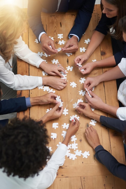 Trouver des solutions pièce par pièce Prise de vue en grand angle d'un groupe d'hommes d'affaires construisant un puzzle ensemble dans un bureau