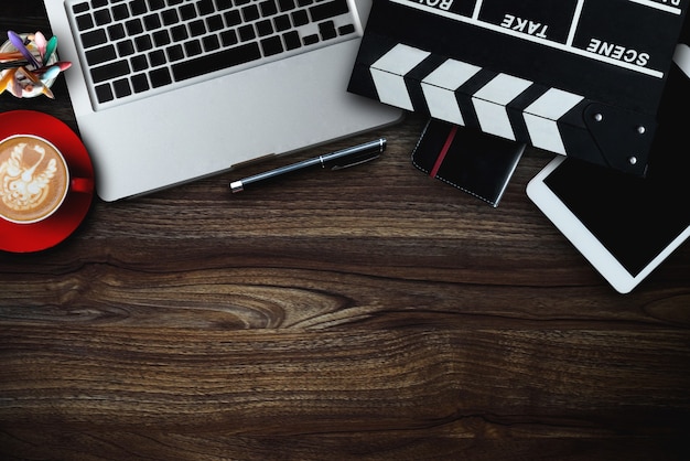 Des trucs de bureau avec Movie clapper, ordinateur portable, smartphone, tablette, tasse à café, stylo, bloc-notes et documents sur la vue de dessus de la table en bois.