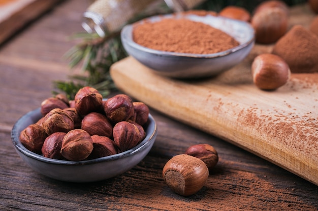 Truffes au chocolat maison, noisettes, amandes et poudre de cacao sur planche à découper en bois. Décoration de vacances d'hiver.