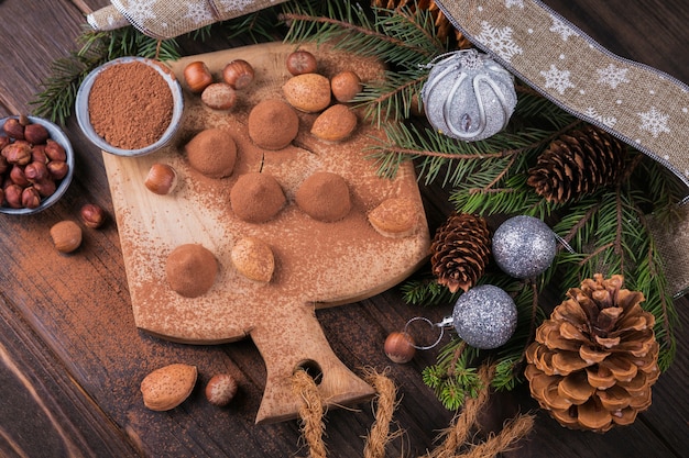 Truffes au chocolat maison, noix, amandes et poudre de cacao sur planche à découper en bois. Décoration de vacances d'hiver.