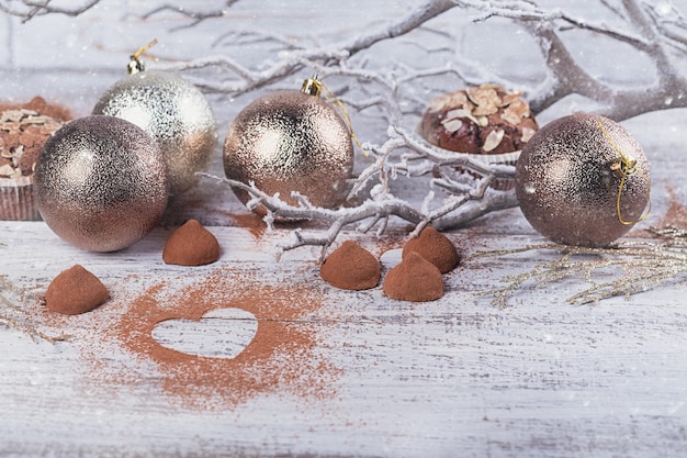 Truffes au chocolat noir faites maison avec de la poudre de cacao en forme de coeur et une décoration d'hiver sur une table en bois rustique blanche. Fond de vacances d'hiver.