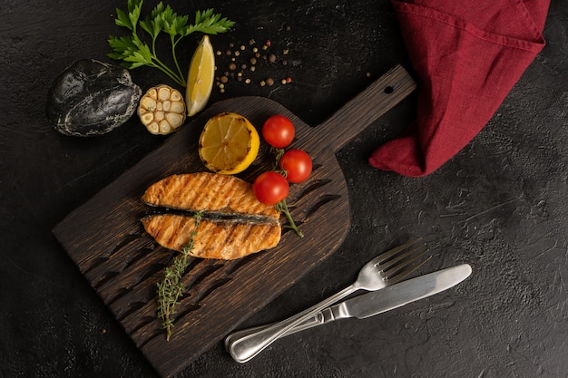 Truite grillée ou filet de saumon aux tomates cerises, citron, ail et thym. Plat de fruits de mer chaud sur un tableau noir. Vue de dessus.