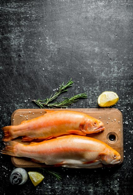 Truite de poisson crue sur une planche à découper en bois avec des tranches de citron et du romarin